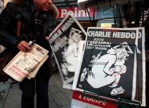 A man takes a copy of the latest edition of French weekly newspaper Charlie Hebdo with the title "One year on, The assassin still on the run" displayed at a kiosk in Nice, France, January 6, 2016. France this week commemorates the victims of last year's Islamist militant attacks on satirical weekly Charlie Hebdo and a Jewish supermarket with eulogies, memorial plaques and another cartoon lampooning religion.      REUTERS/Eric Gaillard  - RTX218G7